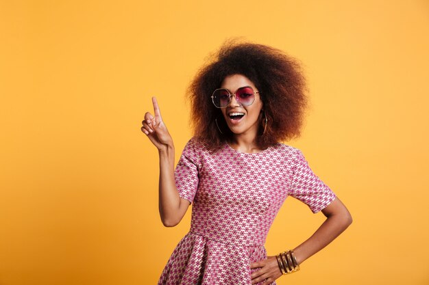 Mujer retro afroamericana bonita con peinado afro apuntando con el dedo hacia arriba