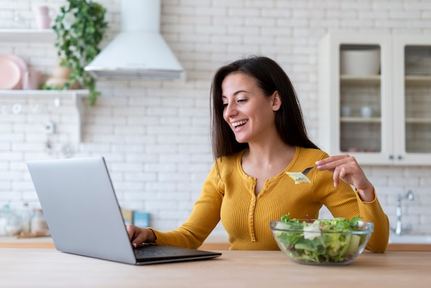 Mujer revisando laptop y comiendo ensalada