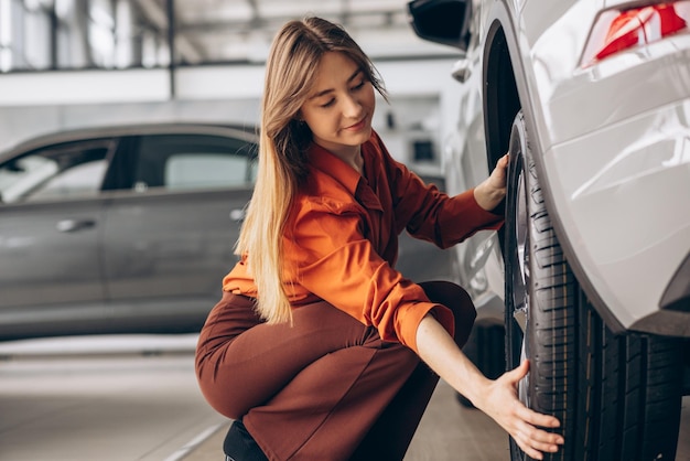 Mujer revisando neumáticos en un automóvil parado en una sala de exposición de automóviles