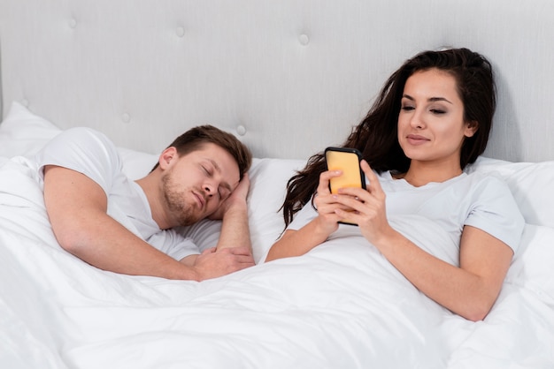 Foto gratuita mujer revisando su teléfono junto al novio dormido
