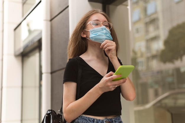Mujer revisando su teléfono mientras usa una máscara médica al aire libre