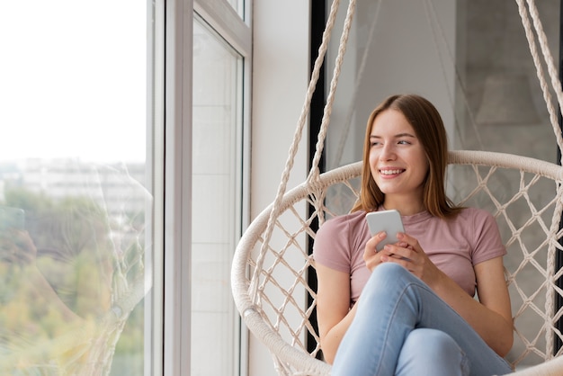 Mujer revisando su teléfono y mirando por la ventana