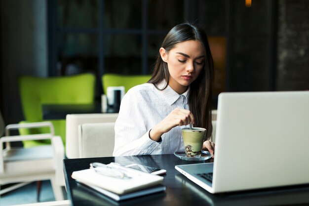 Mujer revolviendo el café en la computadora portátil