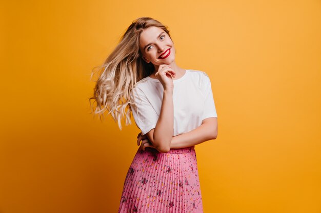 Mujer riendo alegre con cabello rubio. Foto interior de linda chica en falda rosa sonriendo en la pared amarilla.