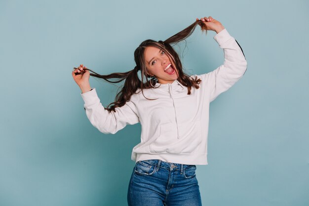 Mujer riendo divertida jugando con su cabello haciendo muecas y bailando sobre pared aislada