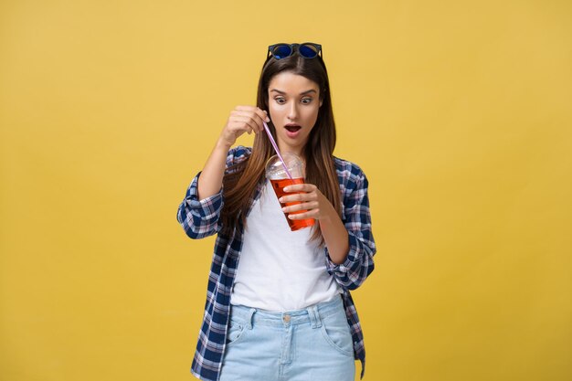 Mujer riendo feliz vistiendo un paño casual bebiendo un cóctel tropical aislado sobre fondo amarillo