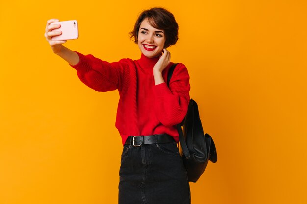 Mujer riendo con mochila posando en la pared amarilla