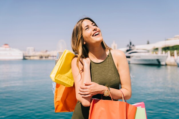 Mujer riéndose y posando con bolsas de compras en el puerto