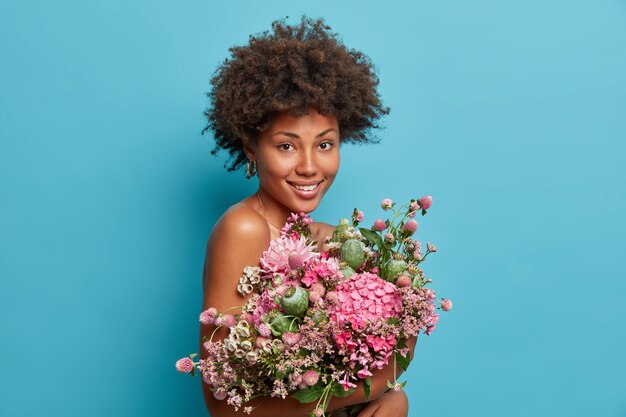 Mujer rizada de aspecto agradable recibe un regalo natural, lleva un hermoso ramo de flores