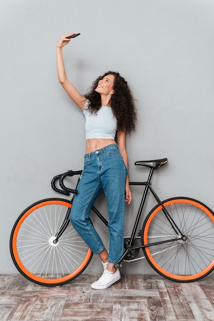 Foto gratuita mujer rizada haciendo selfie en smartphone con bicicleta