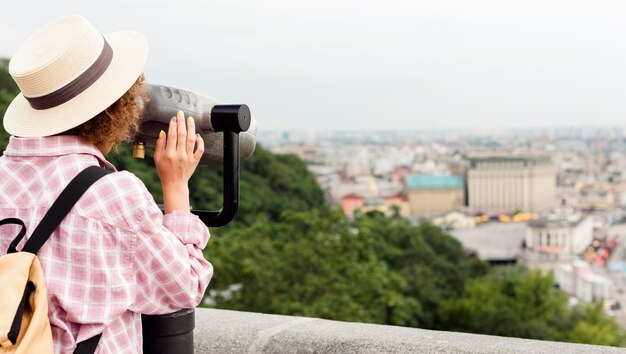 Mujer rizada mirando la ciudad a través de un telescopio con espacio de copia
