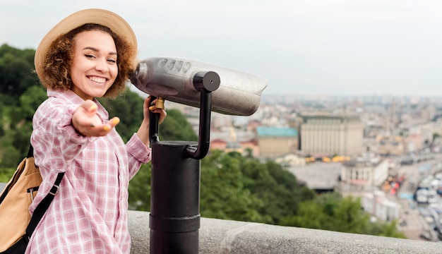 Mujer rizada mirando la ciudad a través de un telescopio