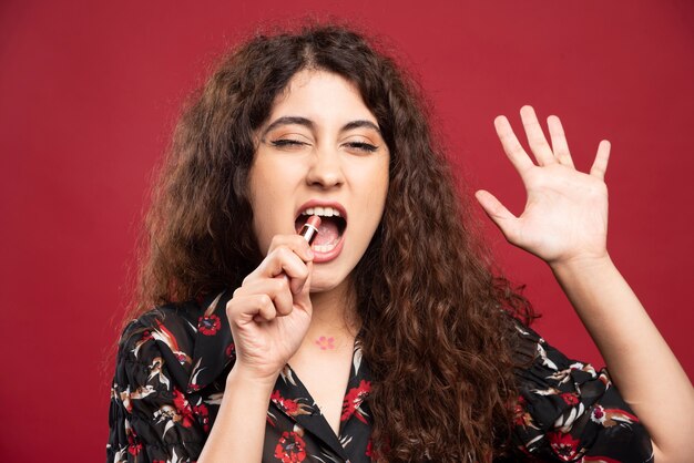 Mujer rizada mordiendo lápiz labial.