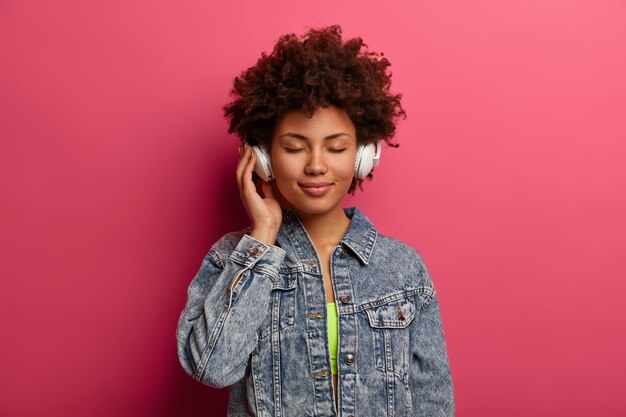 Mujer rizada relajada escucha música en nuevos auriculares estéreo