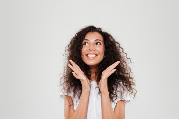 Mujer rizada sonriente con las manos cerca de la cabeza mirando hacia arriba