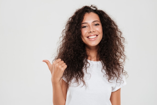 Mujer rizada sonriente que muestra el pulgar para arriba