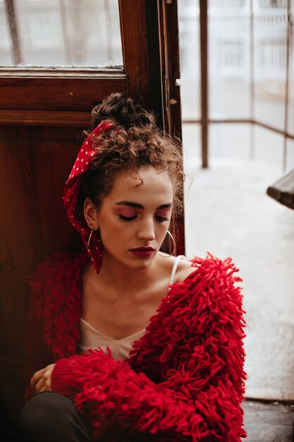 Mujer rizada en suéter rojo posa junto a la puerta de madera