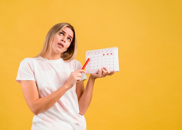 Mujer rodando los ojos y mostrando el calendario de la menstruación