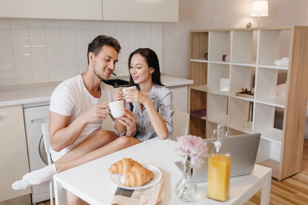 Mujer romántica en calcetines blancos relajándose con su marido durante el desayuno y disfrutando de croissants