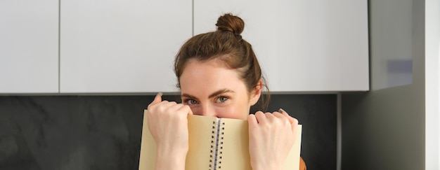 Foto gratuita mujer romántica linda escondiendo la cara detrás de un cuaderno sonriendo con los ojos