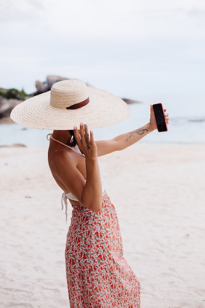 Mujer romántica en la playa en falda de punto superior y sombrero de paja
