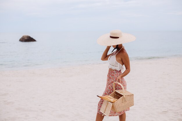 Mujer romántica en la playa en la parte superior de la falda de punto y sombrero de paja con canasta con pan Eco vida