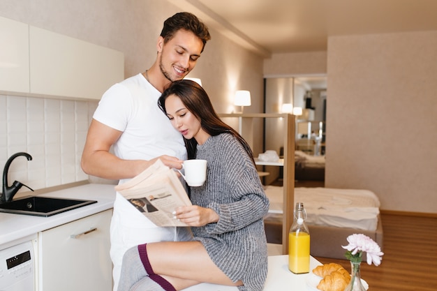 Mujer romántica en vestido de punto leyendo el periódico y abrazando a marido