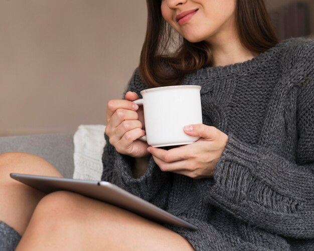 Mujer en ropa acogedora con taza y tableta