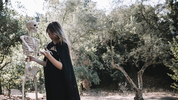 Foto gratuita mujer en ropa de bruja que sostiene con precisión el esqueleto