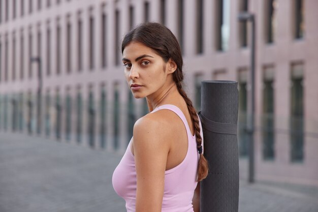 Mujer en ropa deportiva regresa después de entrenar en el club viste ropa deportiva paseos en la ciudad pasa por algunos edificios asiste a la formación de lecciones del club de yoga