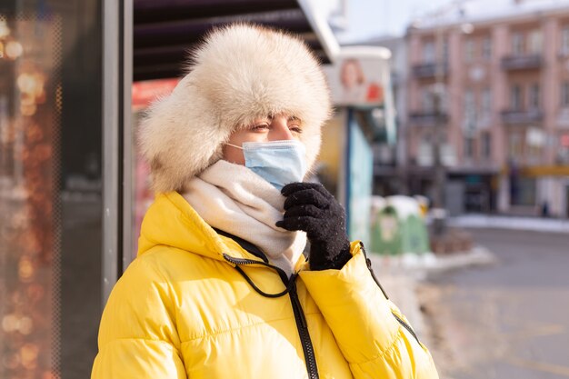 Mujer en ropa de invierno en un día frío esperando un autobús en una parada de autobús