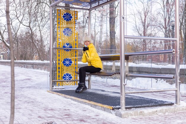 Mujer en ropa de invierno en un día frío esperando un autobús en una parada de autobús