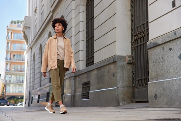 mujer en ropa de moda camina al aire libre pasa por antiguos edificios arquitectónicos concentrados lejos contras de larga distancia a pie. Concepto de estilo de vida urbano