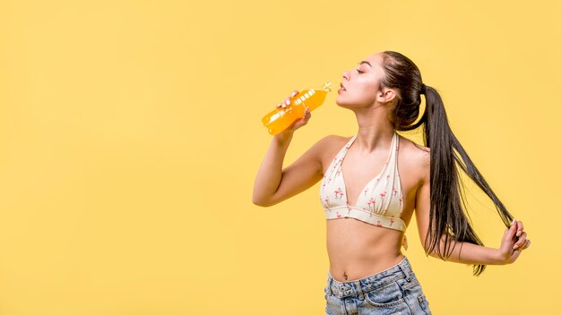 Mujer en ropa de playa de pie y beber jugo de naranja