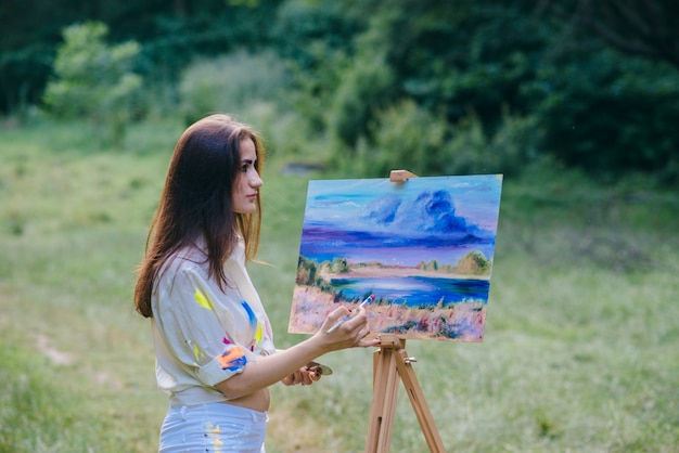 Mujer con la ropa sucia de pintura pintando un cuadro