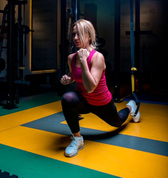 Mujer en rosa haciendo actividades de calentamiento y estiramiento en un gimnasio.