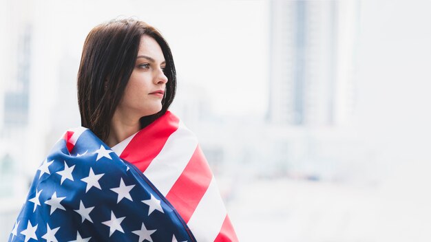 Mujer de rostro sombrío envuelta en bandera americana.