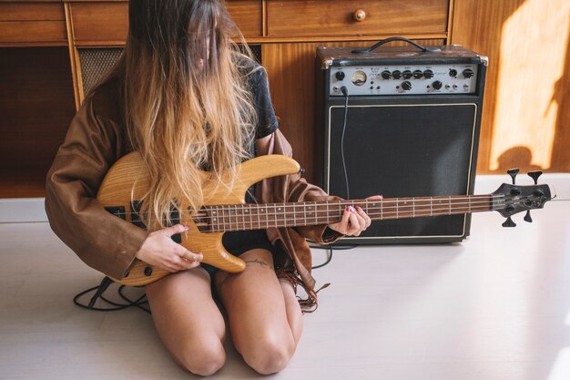 Mujer sin rostro tocando la guitarra en el piso