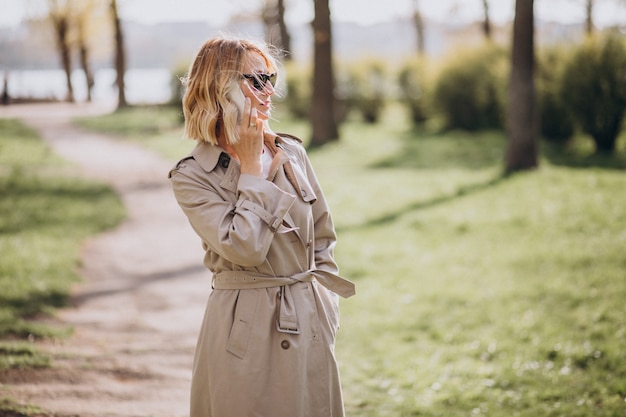 Mujer rubia en abrigo afuera en el parque usando el teléfono