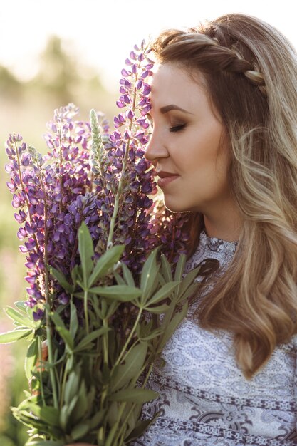 La mujer rubia adorable en vestido azul camina a través del campo de las flores violetas de la lavanda