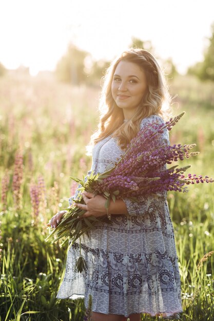 La mujer rubia adorable en vestido azul camina a través del campo de las flores violetas de la lavanda