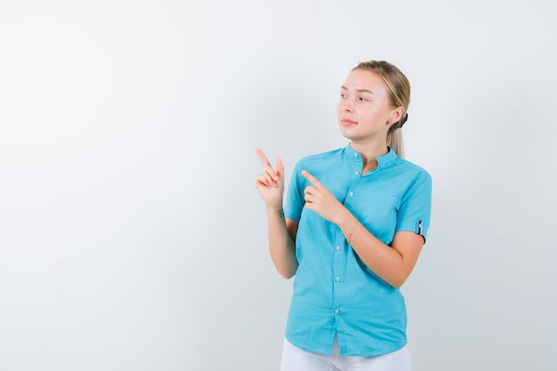 Mujer rubia apuntando a la esquina superior izquierda en blusa azul aislada