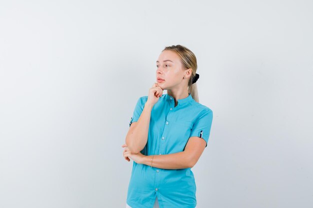 Mujer rubia en blusa azul apoyando la barbilla en la mano y mirando pensativo aislado