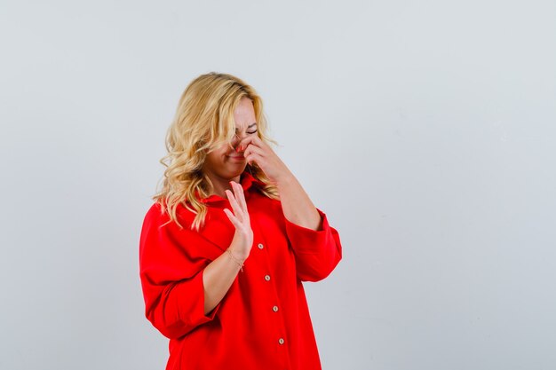 Mujer rubia en blusa roja pellizcando la nariz debido al olor y mirando molesto,