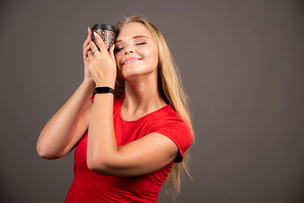 Mujer rubia con café para llevar con expresión feliz.