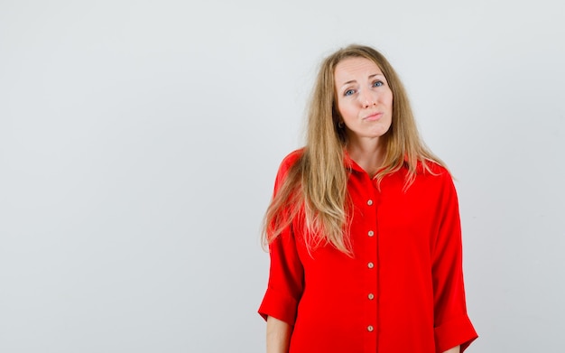 Mujer rubia con camisa roja mirando a cámara y mirando inocente,