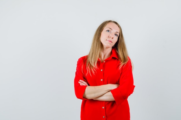 Mujer rubia en camisa roja de pie con los brazos cruzados y mirando confiado,