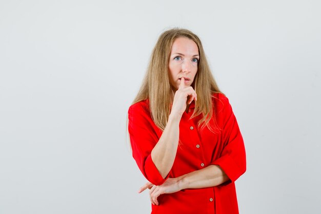 Mujer rubia en camisa roja sosteniendo el dedo en los labios y mirando pensativo,