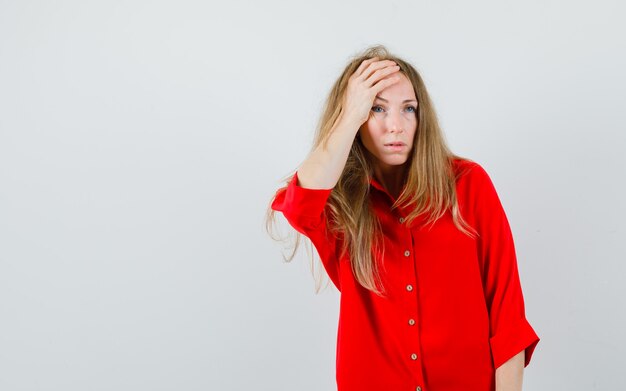 Mujer rubia en camisa roja sosteniendo la mano en la cabeza y mirando triste,