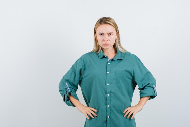 Mujer rubia en camisa verde cogidos de la mano en la cintura y mirando serio